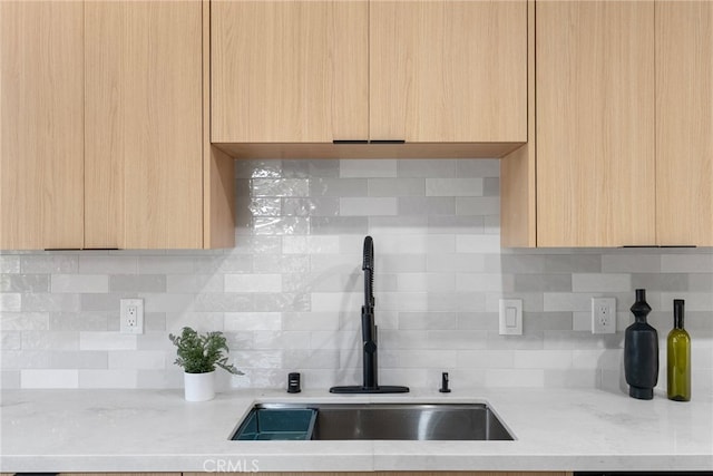 kitchen featuring decorative backsplash, light brown cabinets, light stone countertops, and sink