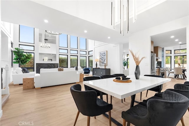 dining space with a healthy amount of sunlight, light wood-type flooring, a high ceiling, and a chandelier