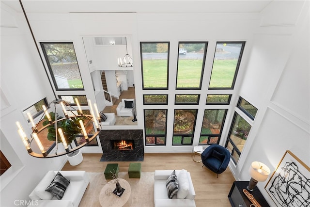 living room with an inviting chandelier, a premium fireplace, a towering ceiling, hardwood / wood-style flooring, and ornamental molding