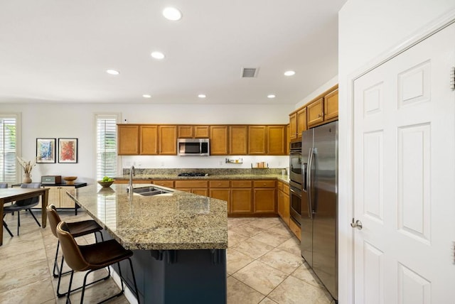 kitchen featuring a breakfast bar, sink, a kitchen island with sink, light stone countertops, and appliances with stainless steel finishes