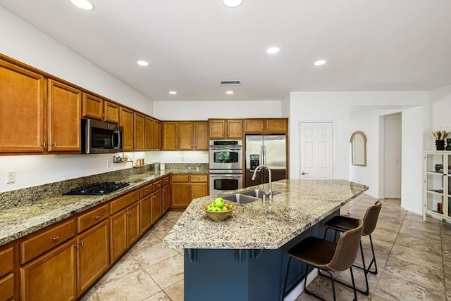 kitchen featuring light stone countertops, a kitchen bar, stainless steel appliances, sink, and a center island with sink