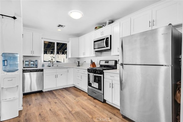 kitchen with white cabinets, light wood-type flooring, appliances with stainless steel finishes, and sink