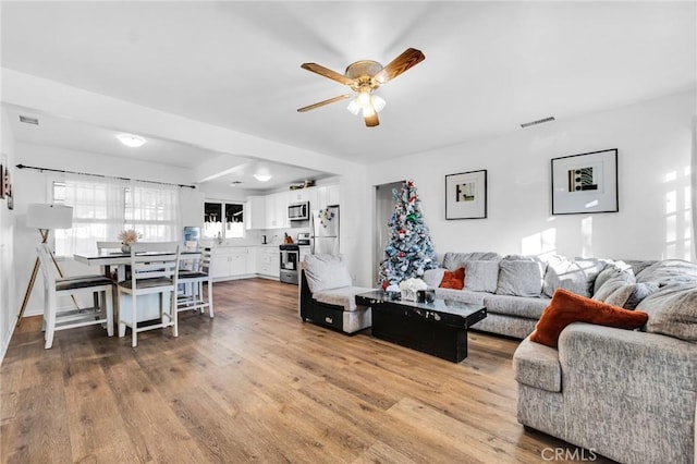 living area with a ceiling fan, visible vents, and wood finished floors