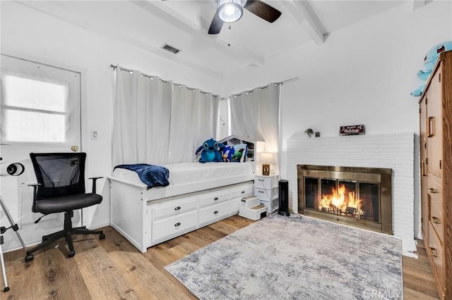 bedroom with ceiling fan, a fireplace, beamed ceiling, and light hardwood / wood-style floors