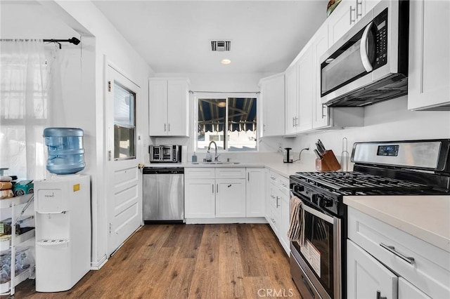 kitchen with appliances with stainless steel finishes, dark hardwood / wood-style flooring, white cabinets, and sink