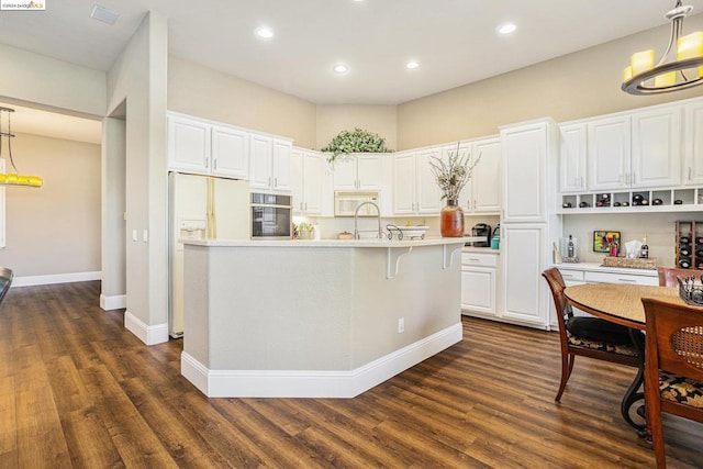 kitchen featuring hanging light fixtures, white cabinetry, a center island with sink, and white appliances