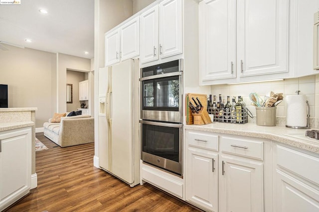 kitchen with dark wood-type flooring, white cabinetry, white fridge with ice dispenser, decorative backsplash, and stainless steel double oven