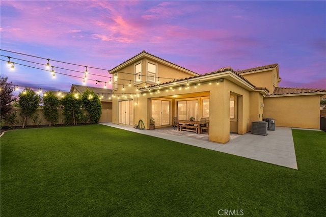 back house at dusk featuring a patio area, a lawn, and central air condition unit