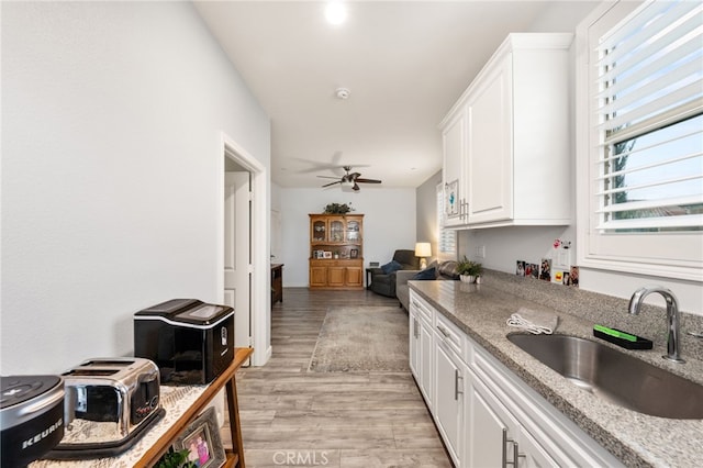 kitchen featuring light hardwood / wood-style flooring, light stone countertops, sink, ceiling fan, and white cabinets