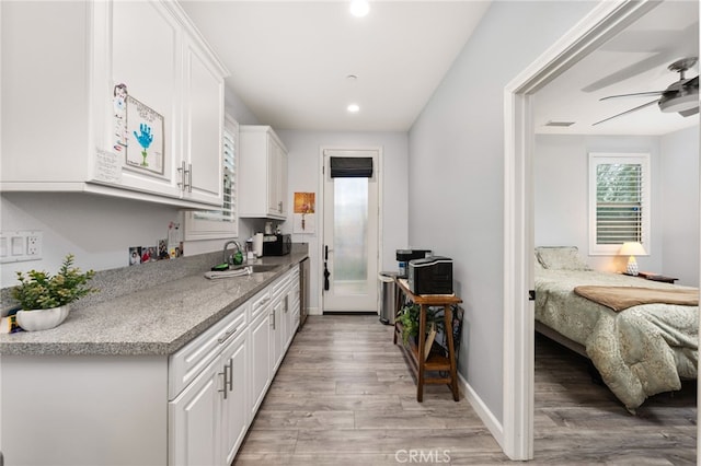 kitchen featuring sink, light stone counters, light wood-type flooring, ceiling fan, and white cabinets