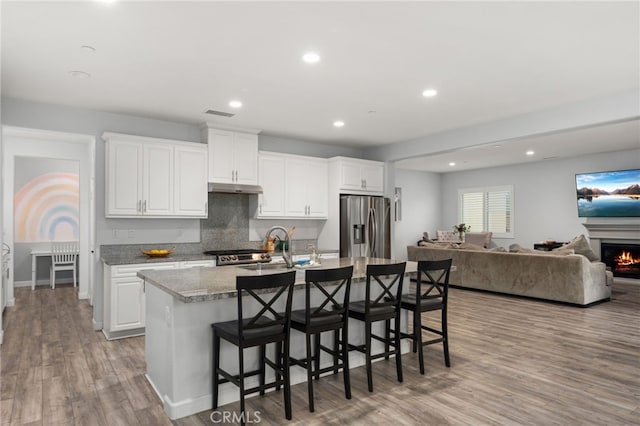 kitchen featuring an island with sink, light wood-type flooring, stainless steel refrigerator with ice dispenser, white cabinets, and a kitchen breakfast bar