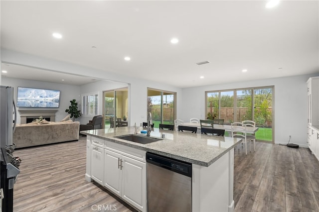 kitchen with a center island with sink, sink, white cabinetry, dishwasher, and light stone countertops