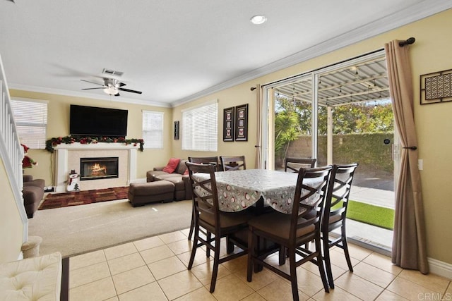 tiled dining space with plenty of natural light, ceiling fan, crown molding, and a tiled fireplace