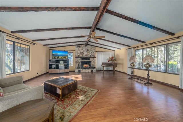 living room with vaulted ceiling with beams, light hardwood / wood-style floors, a stone fireplace, and plenty of natural light