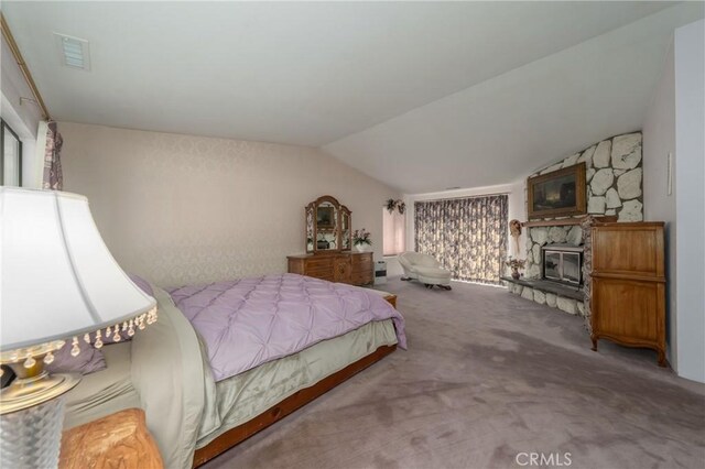 carpeted bedroom with a stone fireplace and vaulted ceiling