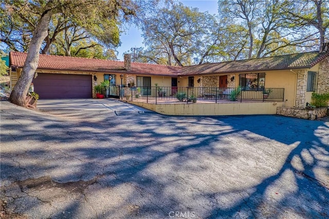 ranch-style house with fence, driveway, stucco siding, stone siding, and a garage