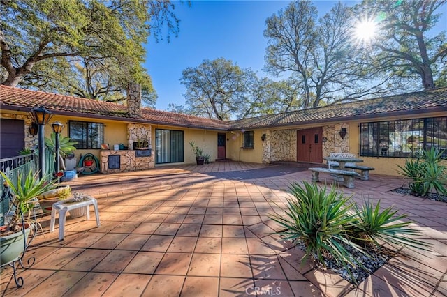 back of house featuring a tiled roof, a patio area, stone siding, and stucco siding