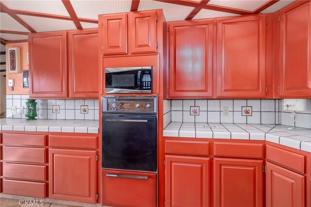 kitchen featuring tile countertops, black oven, tasteful backsplash, and light tile patterned flooring