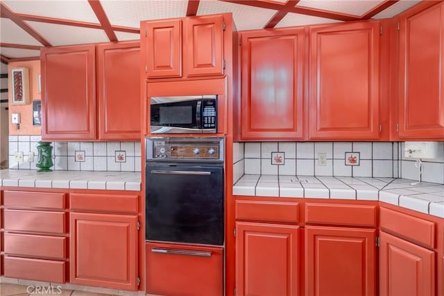 kitchen with tile counters, stainless steel microwave, oven, and decorative backsplash