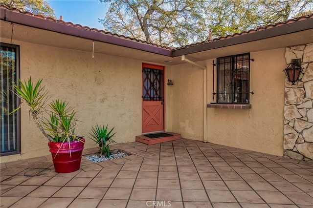 doorway to property featuring a patio, a tile roof, and stucco siding
