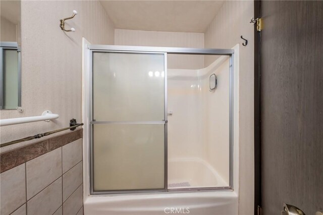 bathroom with bath / shower combo with glass door and tile walls