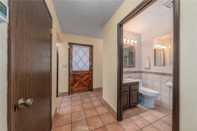 bathroom featuring tile patterned floors, a textured ceiling, toilet, vanity, and tile walls