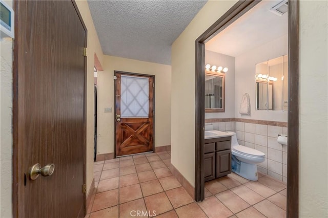bathroom with vanity, a textured ceiling, tile patterned floors, toilet, and tile walls