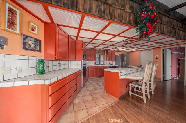 kitchen featuring tile counters, a center island, stainless steel appliances, light hardwood / wood-style flooring, and a kitchen bar