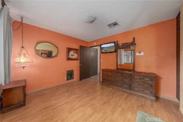bedroom featuring baseboards, wood finished floors, visible vents, and a textured ceiling