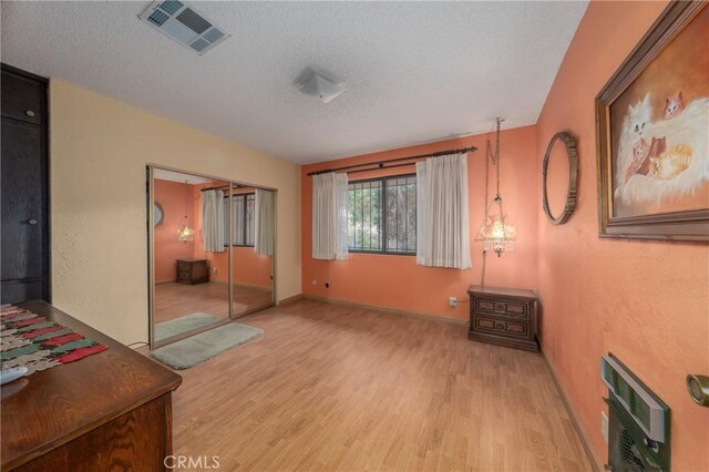 interior space with a textured ceiling, heating unit, light hardwood / wood-style flooring, and a closet