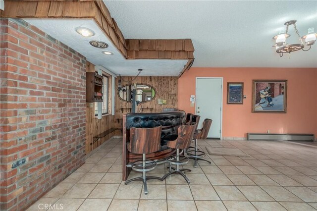 dining area with wood walls, a baseboard heating unit, light tile patterned floors, a textured ceiling, and a notable chandelier