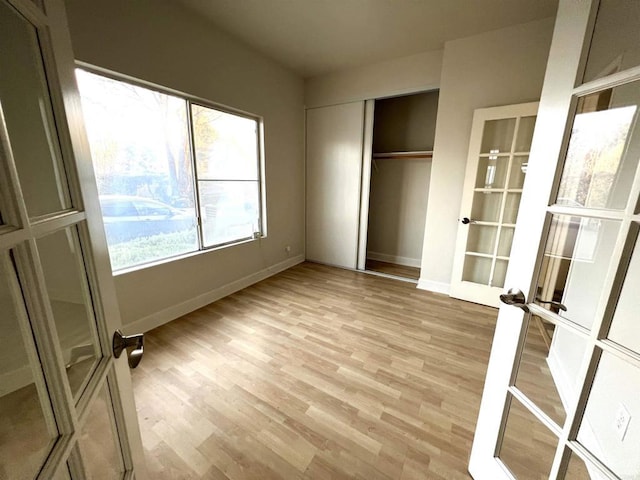 unfurnished bedroom with multiple windows, french doors, and light hardwood / wood-style floors