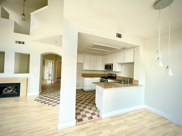 kitchen with a high ceiling, white cabinets, sink, kitchen peninsula, and stainless steel appliances