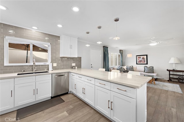 kitchen with kitchen peninsula, light wood-type flooring, stainless steel dishwasher, sink, and decorative light fixtures