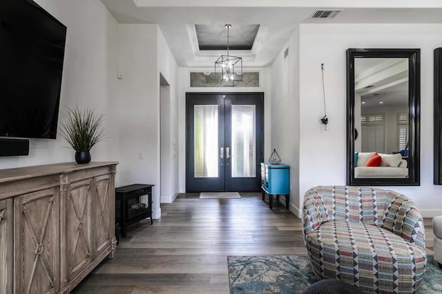 foyer entrance with a notable chandelier, dark hardwood / wood-style floors, a raised ceiling, and french doors