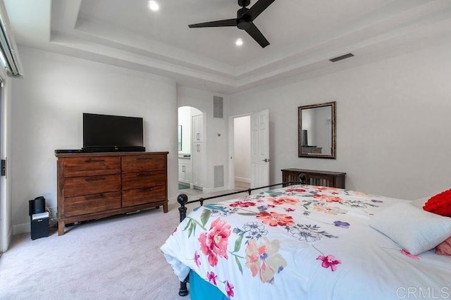 bedroom with a tray ceiling, ensuite bath, ceiling fan, and light colored carpet