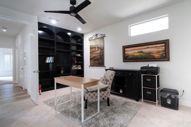 office space with built in shelves, ceiling fan, and light colored carpet