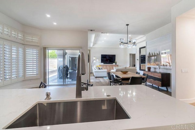 kitchen with visible vents, light stone counters, open floor plan, a chandelier, and a sink