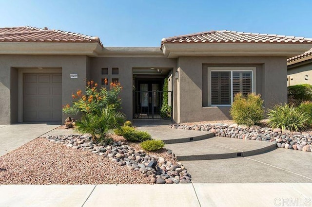 property entrance with an attached garage, driveway, a tiled roof, and stucco siding