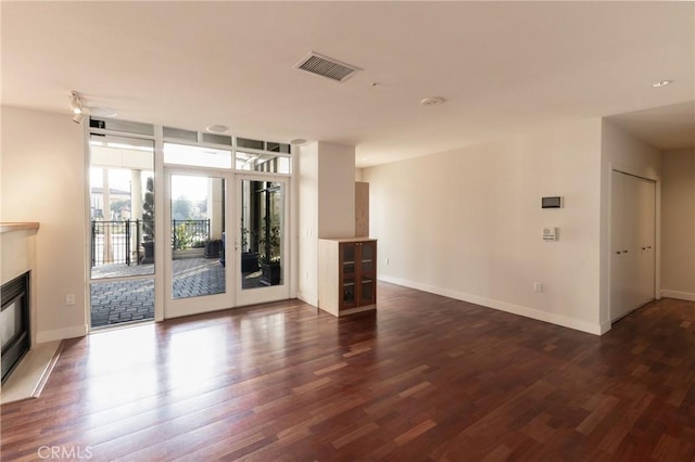unfurnished living room with visible vents, dark wood-type flooring, baseboards, and a glass covered fireplace