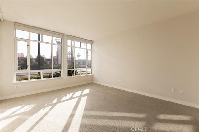 unfurnished room featuring a healthy amount of sunlight, baseboards, and carpet flooring