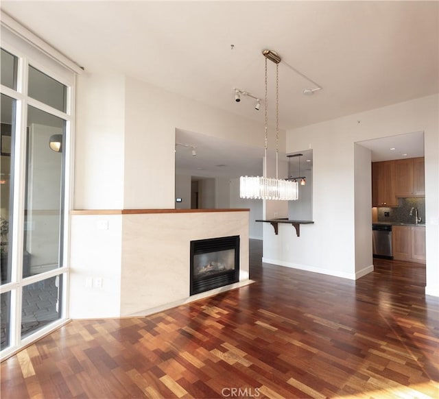unfurnished living room with baseboards, a sink, dark wood-style floors, and a premium fireplace