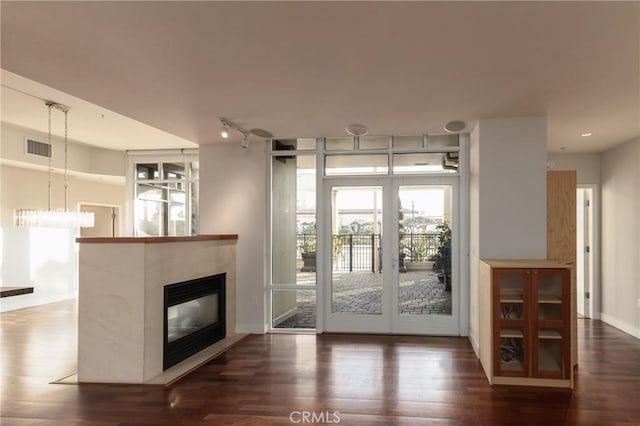 interior space with a glass covered fireplace, rail lighting, wood finished floors, and visible vents