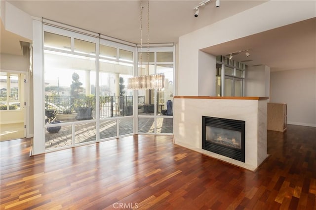 unfurnished living room featuring track lighting, floor to ceiling windows, a glass covered fireplace, and wood finished floors