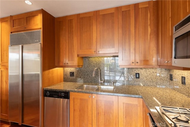 kitchen with brown cabinets, light stone counters, a sink, stainless steel appliances, and tasteful backsplash