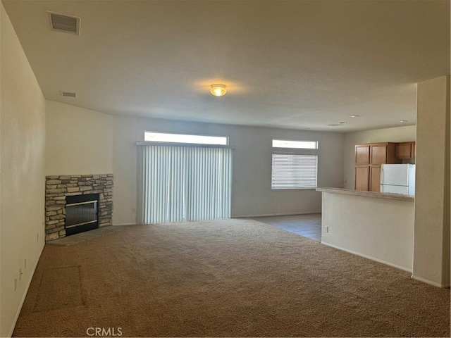 unfurnished living room with a stone fireplace and light colored carpet