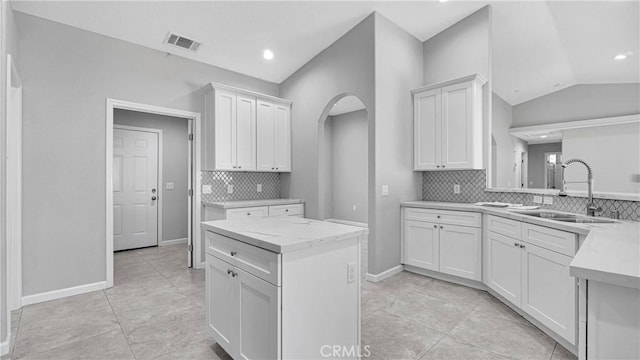 kitchen featuring white cabinets, backsplash, lofted ceiling, and sink