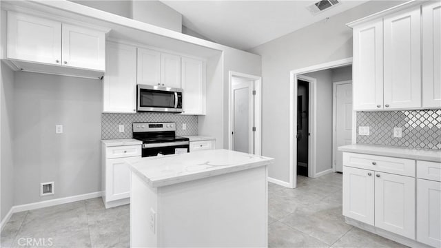 kitchen featuring light stone countertops, appliances with stainless steel finishes, vaulted ceiling, and white cabinetry