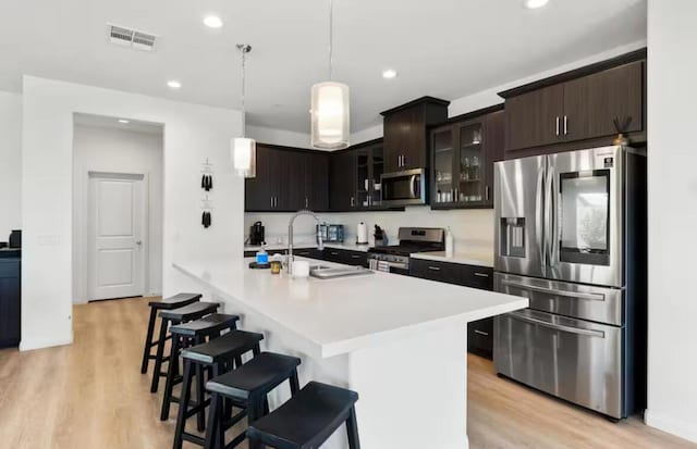 kitchen featuring a kitchen breakfast bar, sink, light wood-type flooring, appliances with stainless steel finishes, and dark brown cabinetry