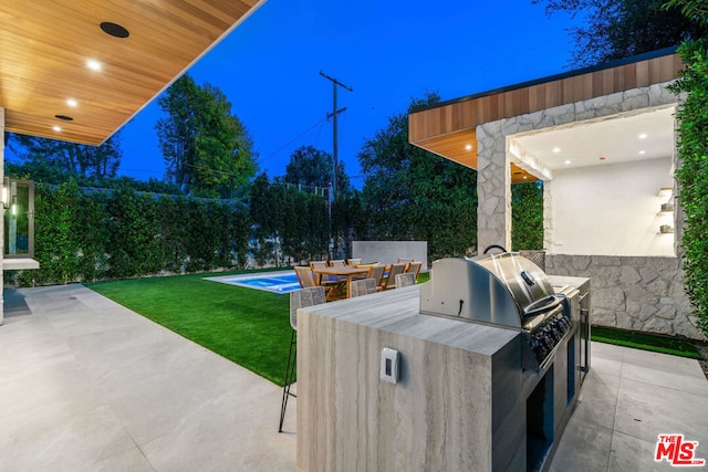 view of patio with area for grilling, a pool, and exterior kitchen